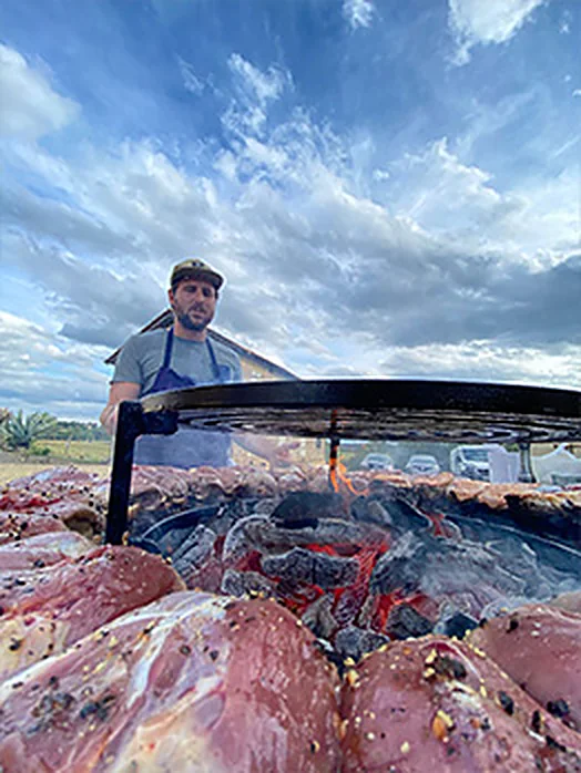 Nicolas Fort devant le brasero chargé de pièces de viande, en plein air